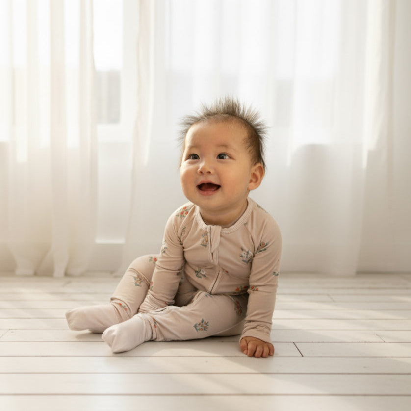Baby sitting on a light wooden floor with white curtains in the background